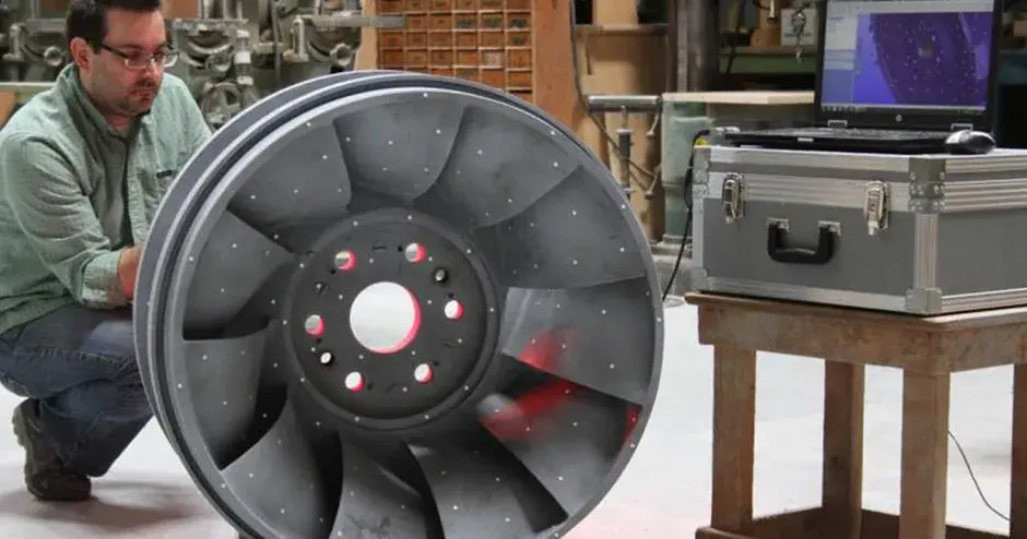 Persona in piedi accanto a una parte ottenuta mediante fusione a cera persa in un contesto industriale