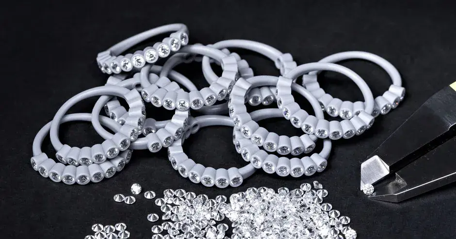 numerosi anelli stampati in cera con diamanti incastonati, punta di un calibro che regge un diamante, diamanti sparsi