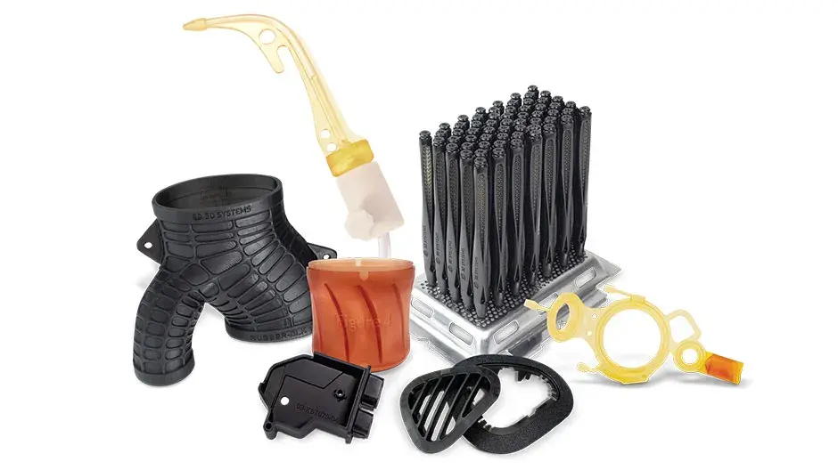 Diversi componenti stampati in 3D sono esposti su uno sfondo blu. Tra questi, un ingranaggio bianco, un modello medico colorato e altri componenti di produzione in tinta unita, neri e grigi.